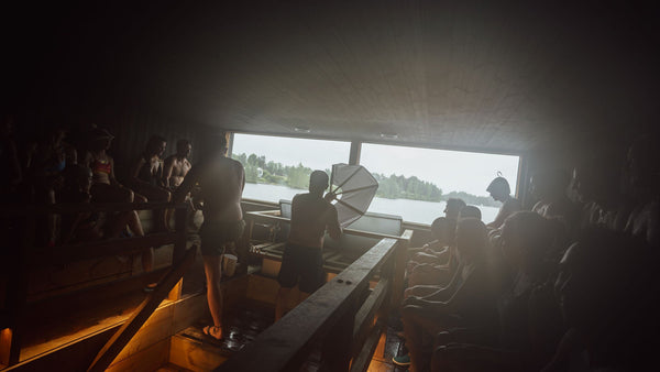 Interior de una sauna finlandesa junto a un lago, con bañistas y vapor (löyly)