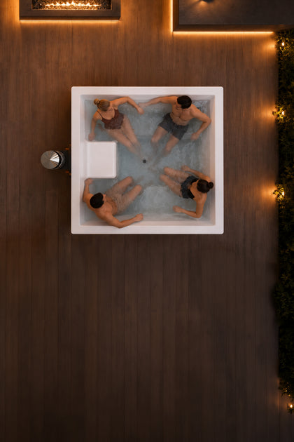 Cuatro personas en una bañera nórdica HILDA sobre terraza de madera oscura con iluminación cálida